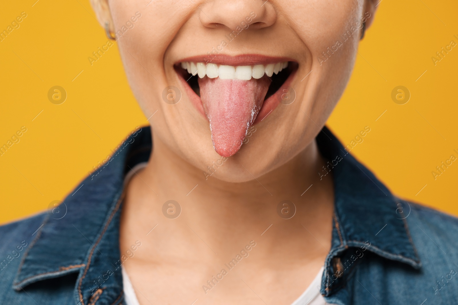 Photo of Happy young woman showing her tongue on yellow background, closeup