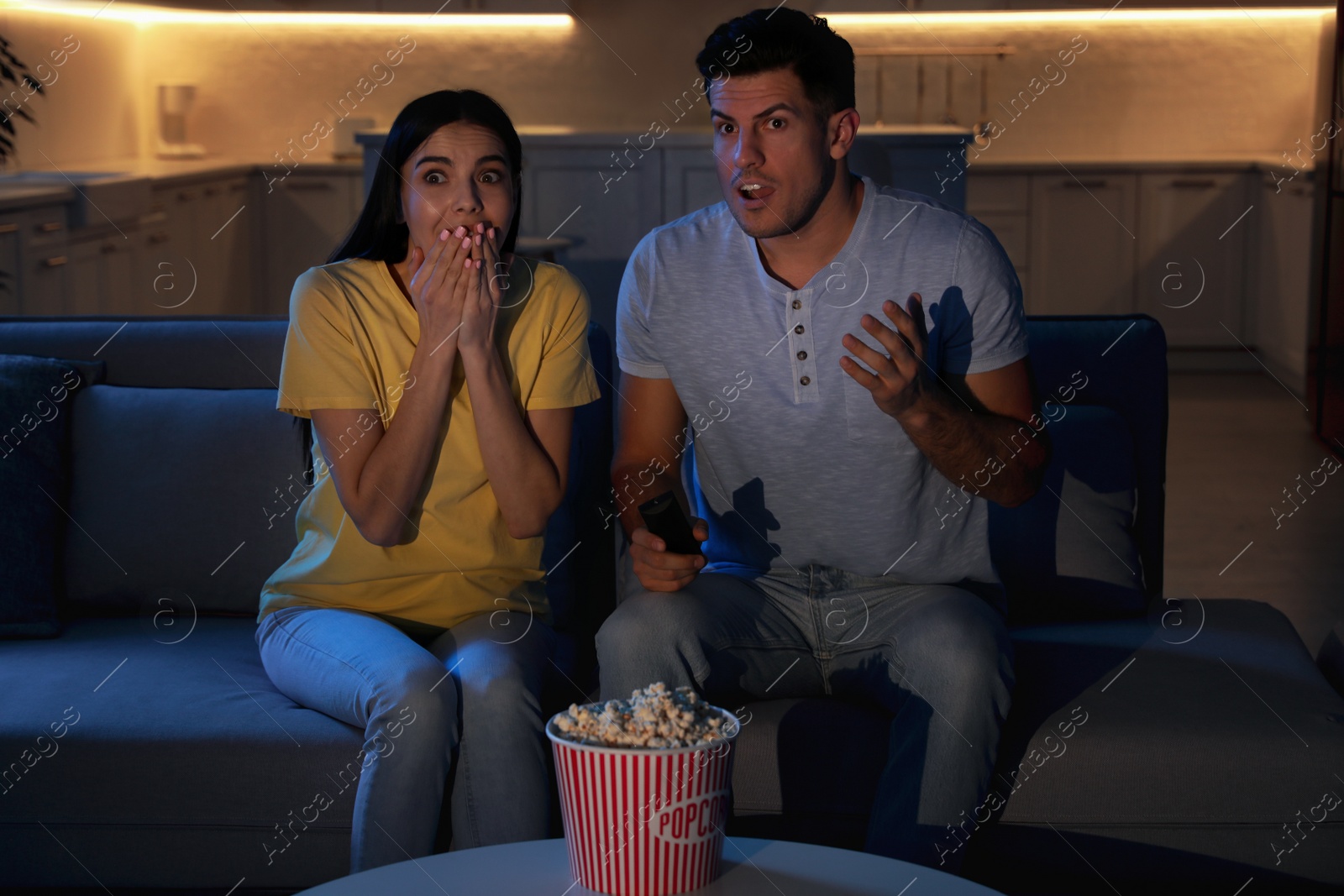 Photo of Couple watching movie with popcorn on sofa at night