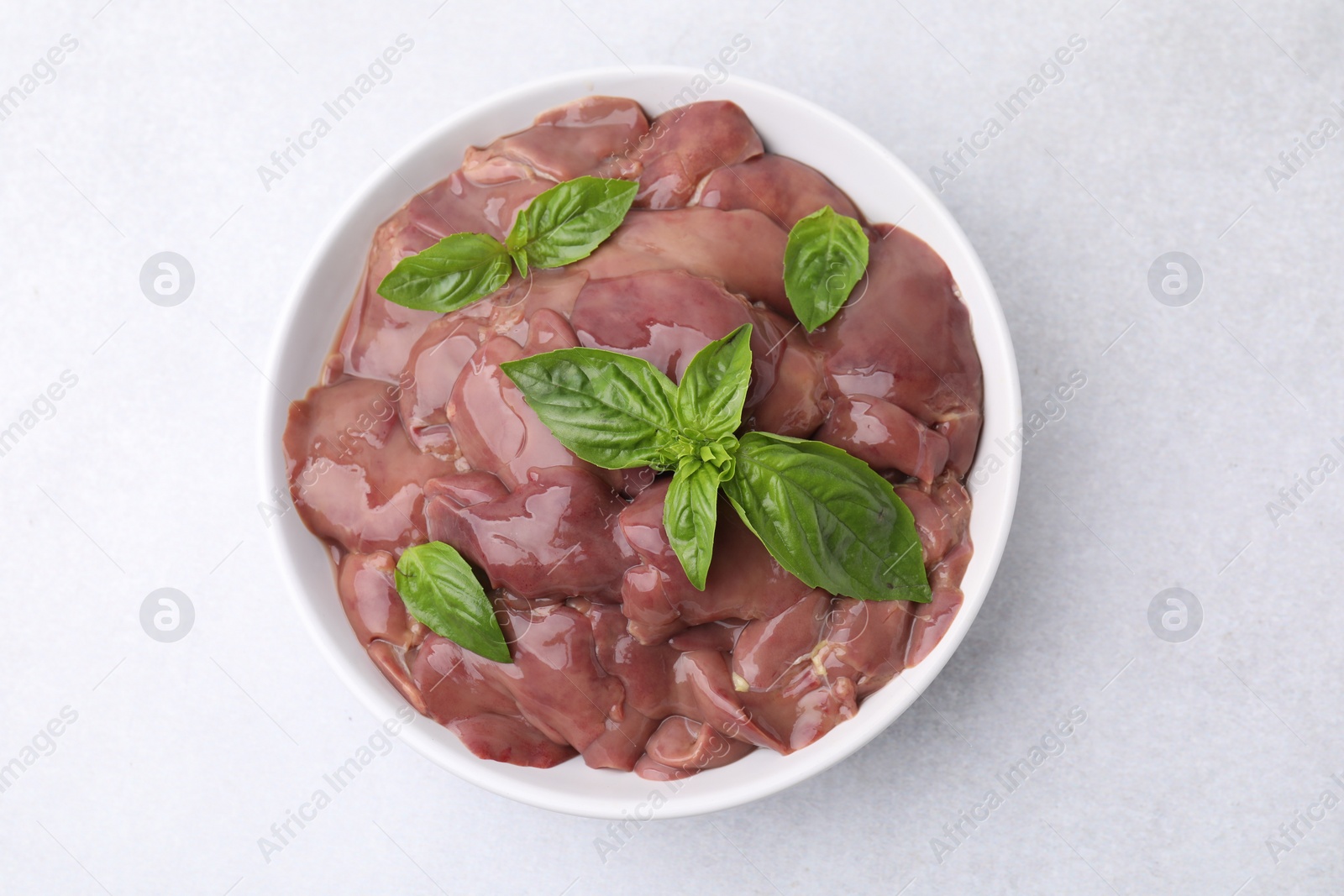 Photo of Bowl with raw chicken liver and basil on white table, top view