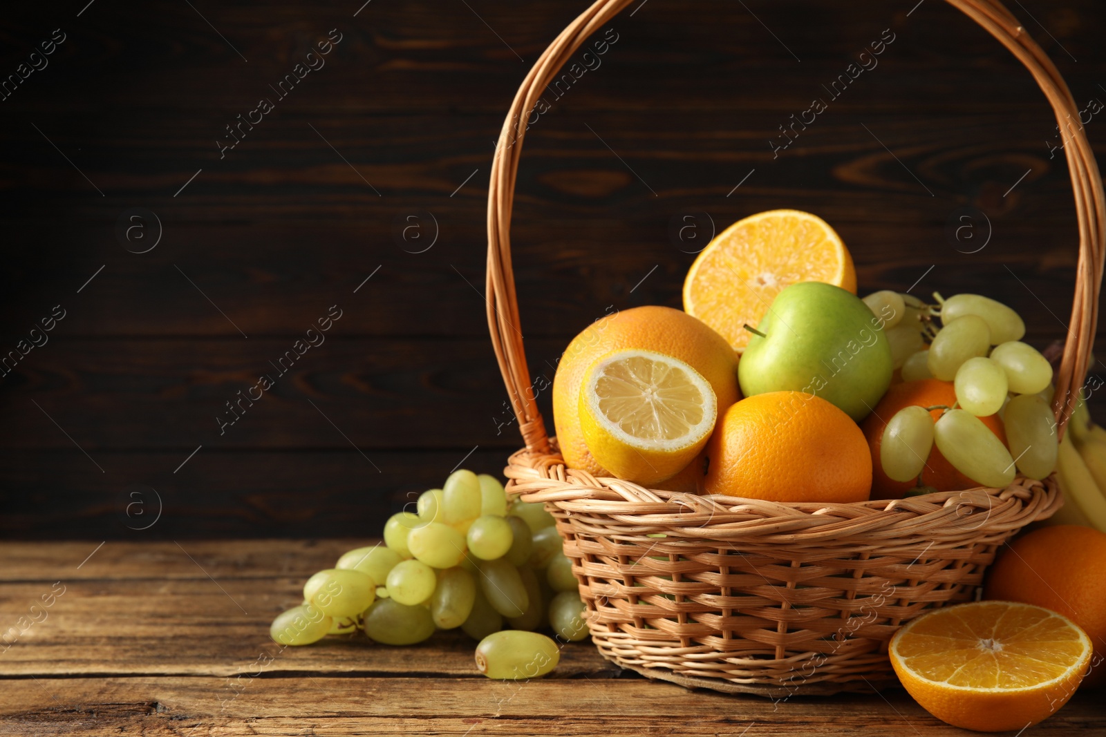 Photo of Wicker basket with different fruits on wooden table. Space for text