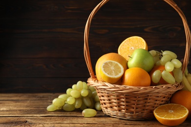 Photo of Wicker basket with different fruits on wooden table. Space for text