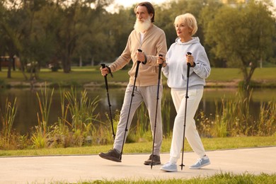 Photo of Senior man and woman performing Nordic walking outdoors, space for text