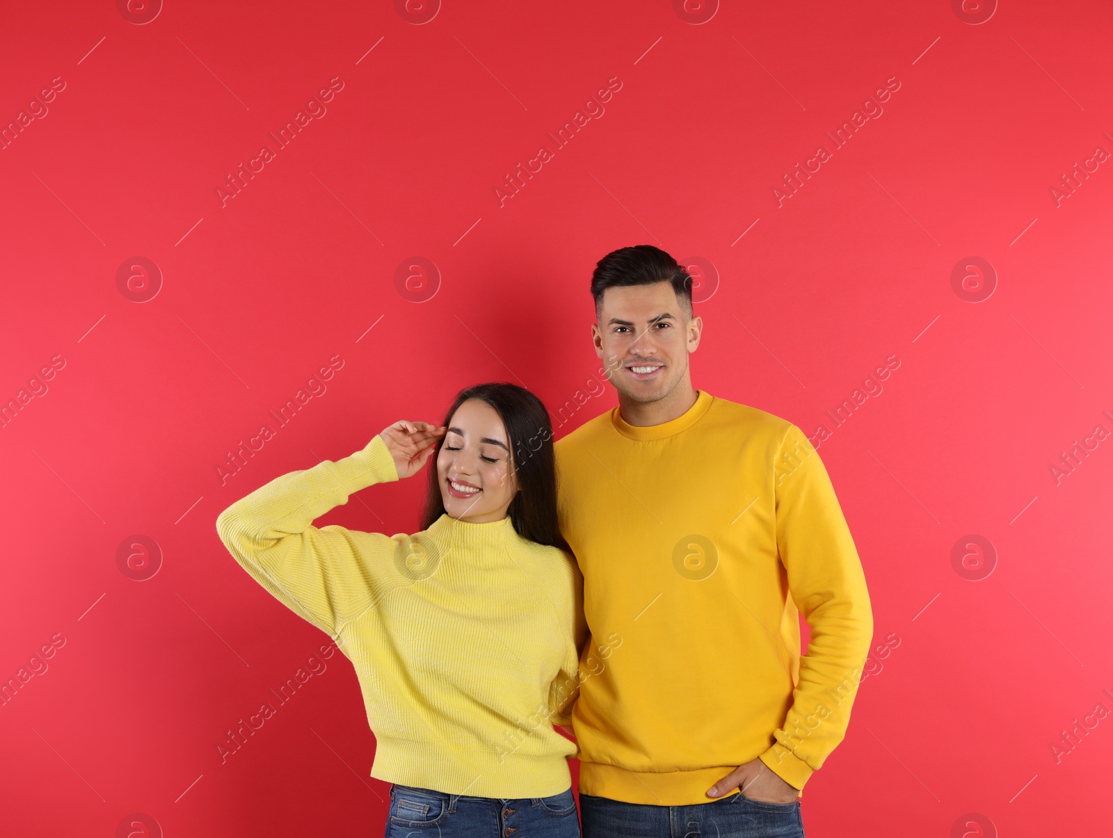 Photo of Happy couple wearing yellow warm sweaters on red background