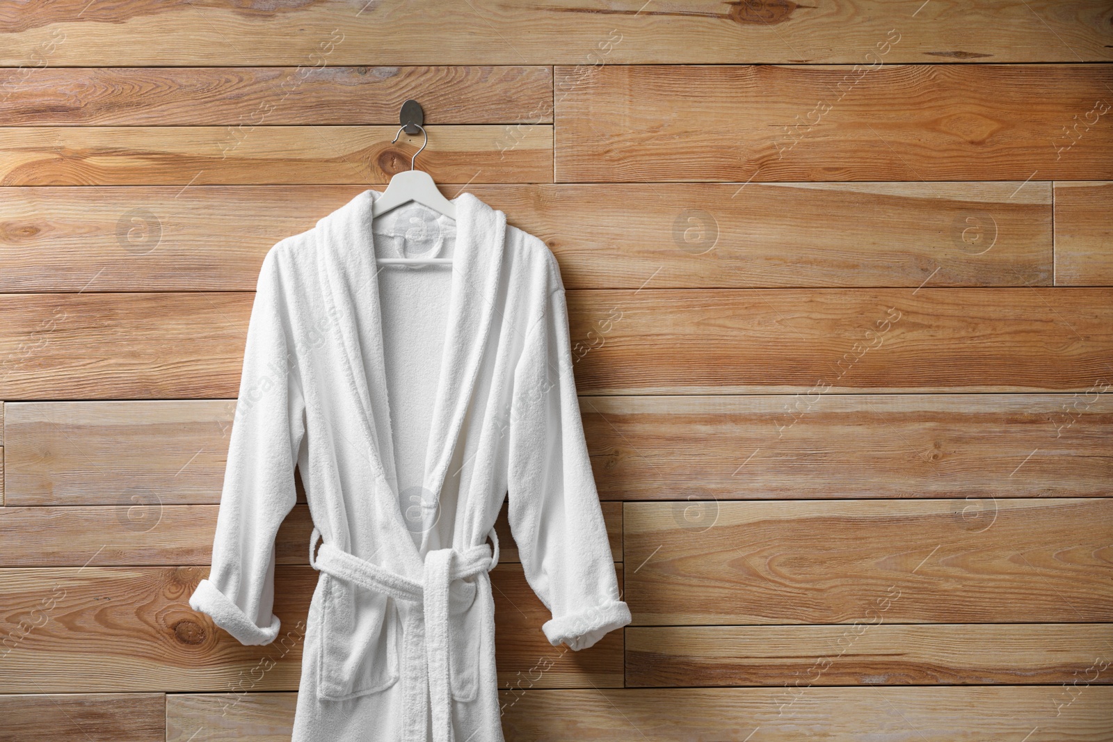 Photo of Soft comfortable bathrobe hanging on wooden wall, space for text