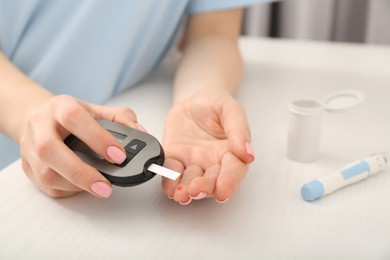 Photo of Diabetes. Woman checking blood sugar level with glucometer at wooden table, closeup