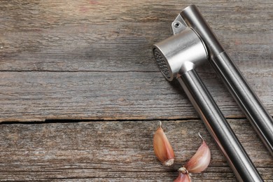 Garlic press and cloves on wooden table, above view. Space for text