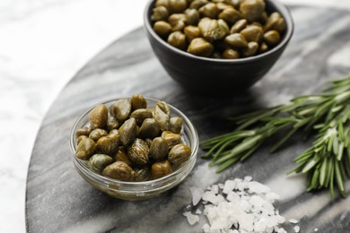 Photo of Delicious pickled capers, salt and rosemary twigs on grey marble board