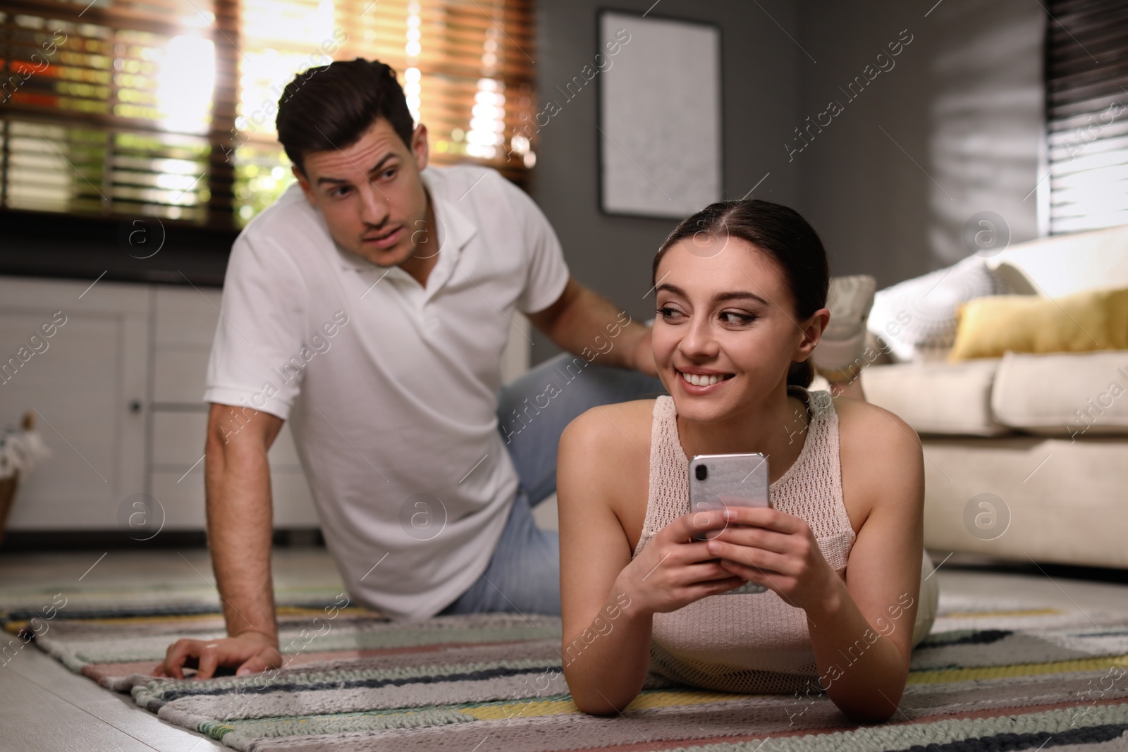 Photo of Couple quarreling due to jealousy in relationship at home, focus on woman with smartphone