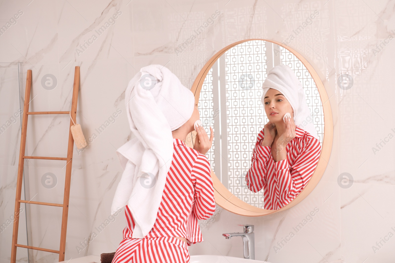 Photo of Young woman with towel on head near mirror in bathroom