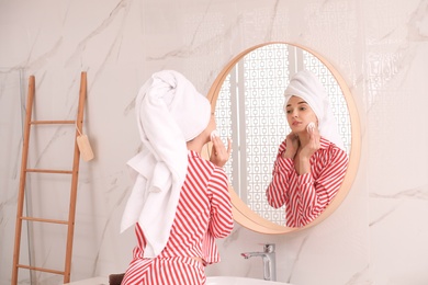 Young woman with towel on head near mirror in bathroom