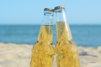 Photo of Bottles of cold beer on beach near sea, closeup