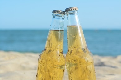 Bottles of cold beer on beach near sea, closeup