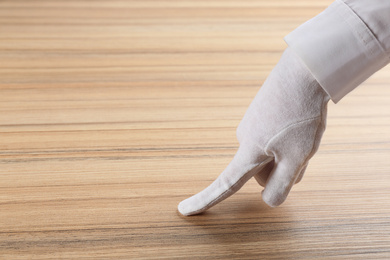 Photo of Person in white glove checking cleanliness of wooden  table, closeup. Space for text