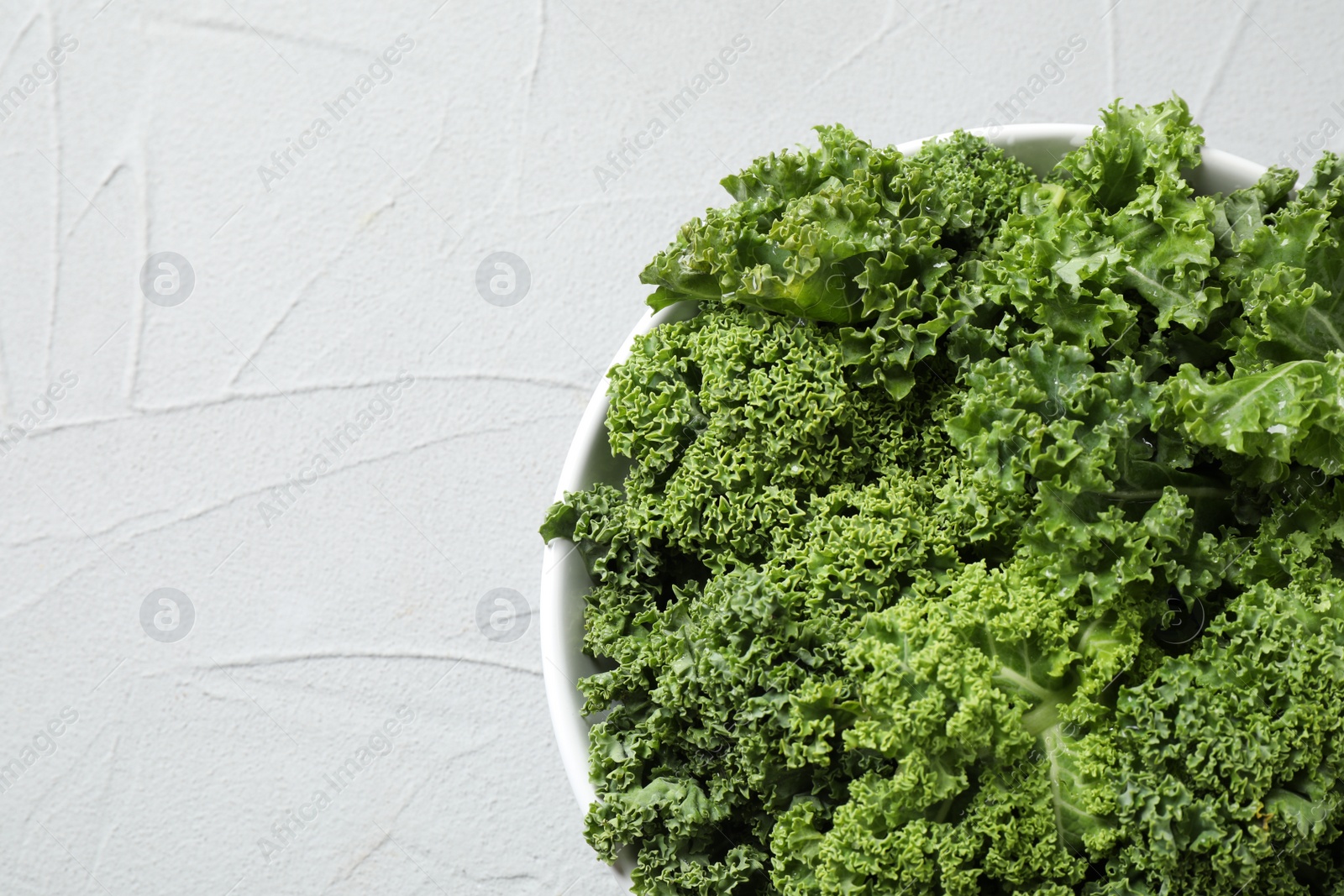 Photo of Fresh kale leaves on white table, top view. Space for text