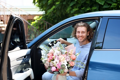 Photo of Young handsome man with beautiful flower bouquet in car