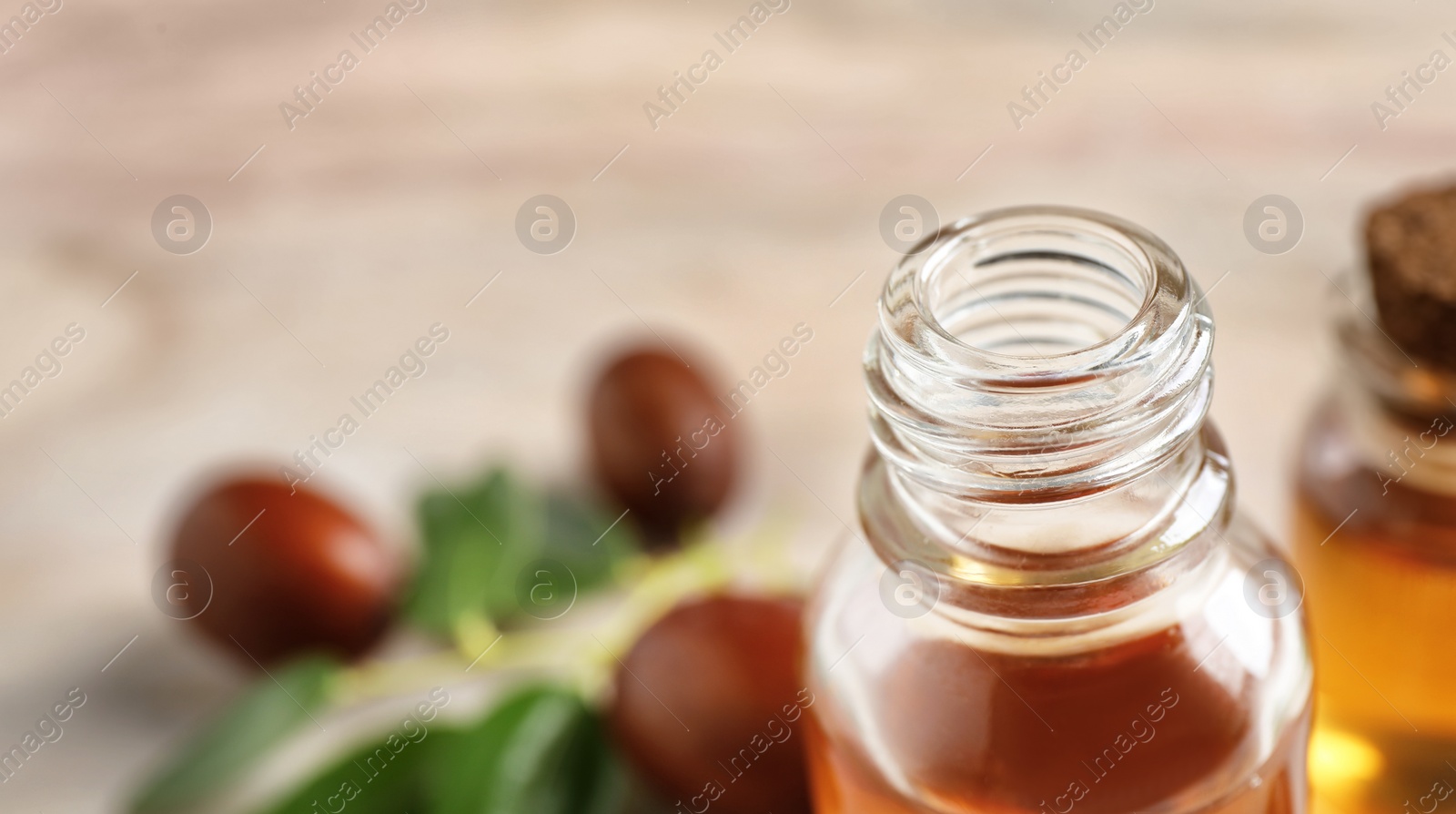 Photo of Glass bottle with jojoba oil on blurred background, closeup. Space for text