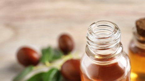 Glass bottle with jojoba oil on blurred background, closeup. Space for text