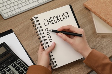 Woman filling Checklist at wooden table, above view