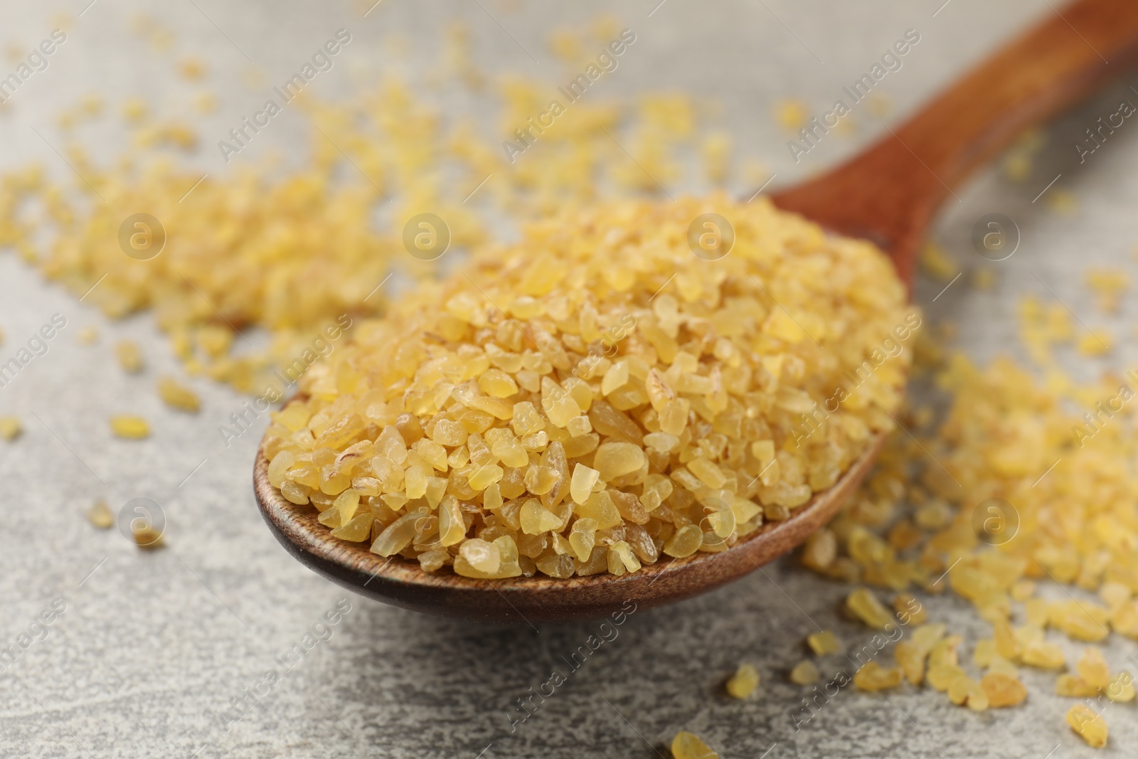 Photo of Spoon with raw bulgur on gray table, closeup