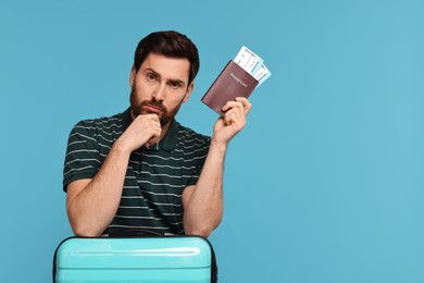 Photo of Thoughtful man with passport, suitcase and tickets on light blue background. Space for text