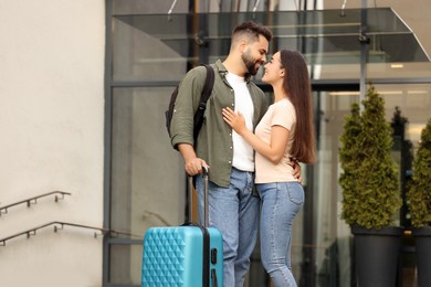 Photo of Long-distance relationship. Beautiful young couple with luggage hugging near building outdoors, low angle view