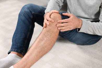Photo of Man suffering from leg pain on white carpet, closeup