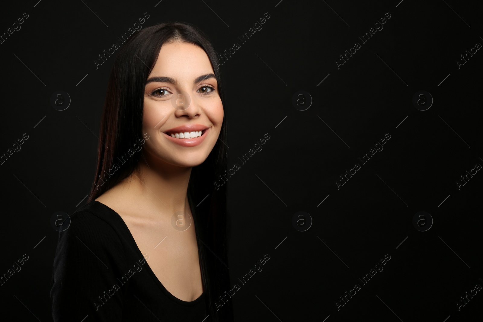 Photo of Portrait of happy young woman with beautiful black hair and charming smile on dark background, space for text