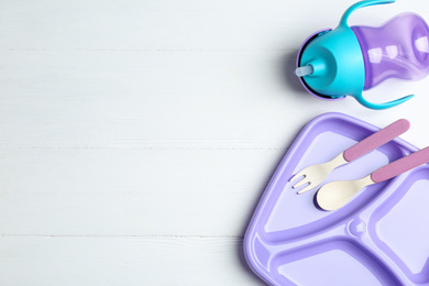 Photo of Set of plastic dishware on white wooden table, flat lay with space for text. Serving baby food