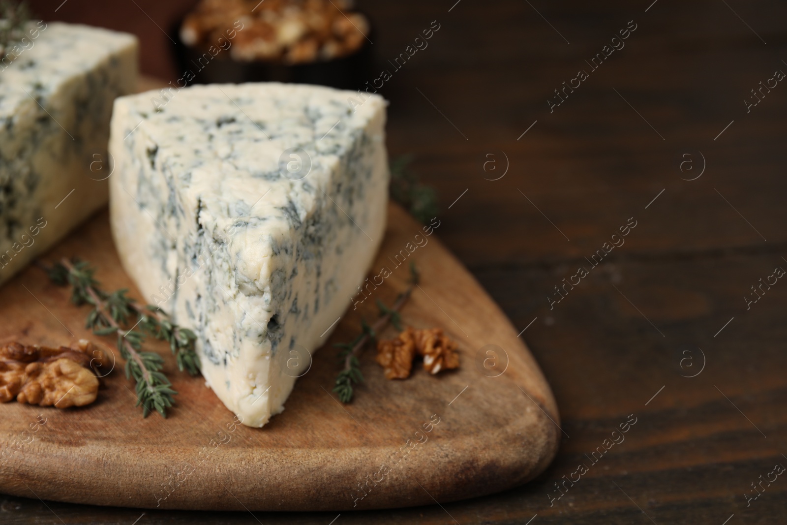 Photo of Tasty blue cheese with thyme and walnuts on wooden table, closeup. Space for text
