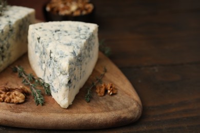 Photo of Tasty blue cheese with thyme and walnuts on wooden table, closeup. Space for text