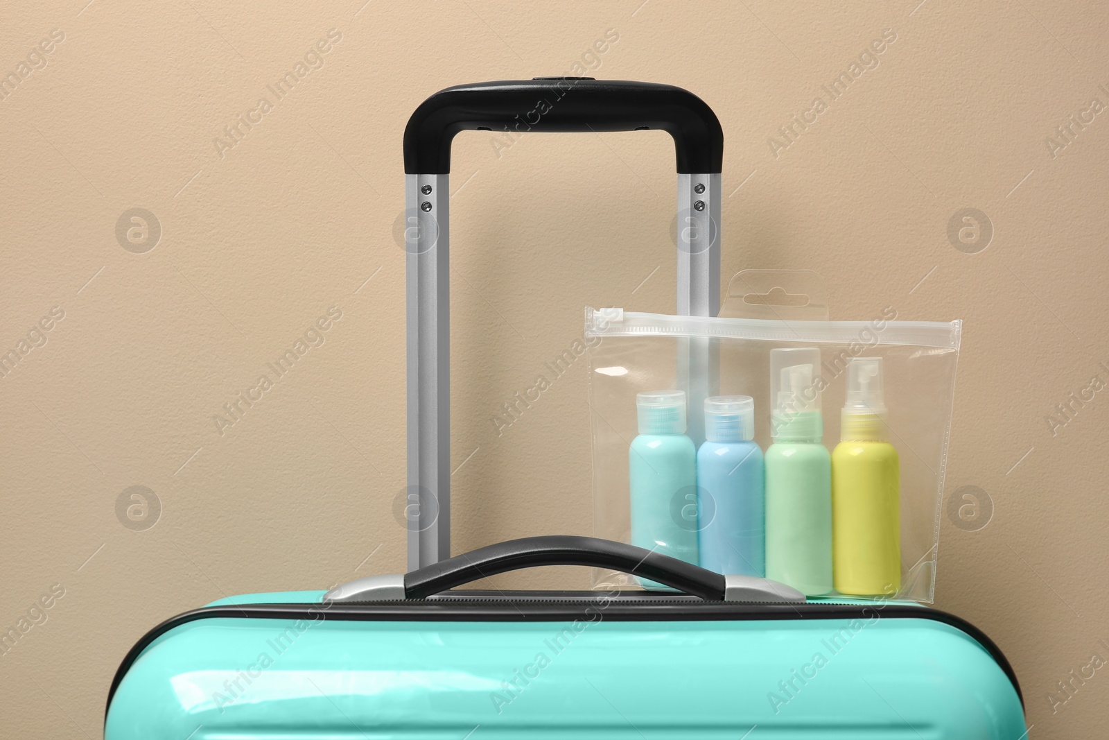 Photo of Cosmetic travel kit in plastic bag on suitcase against beige wall. Bath accessories