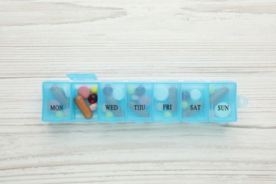 Photo of Pill box with medicaments on white wooden table, top view