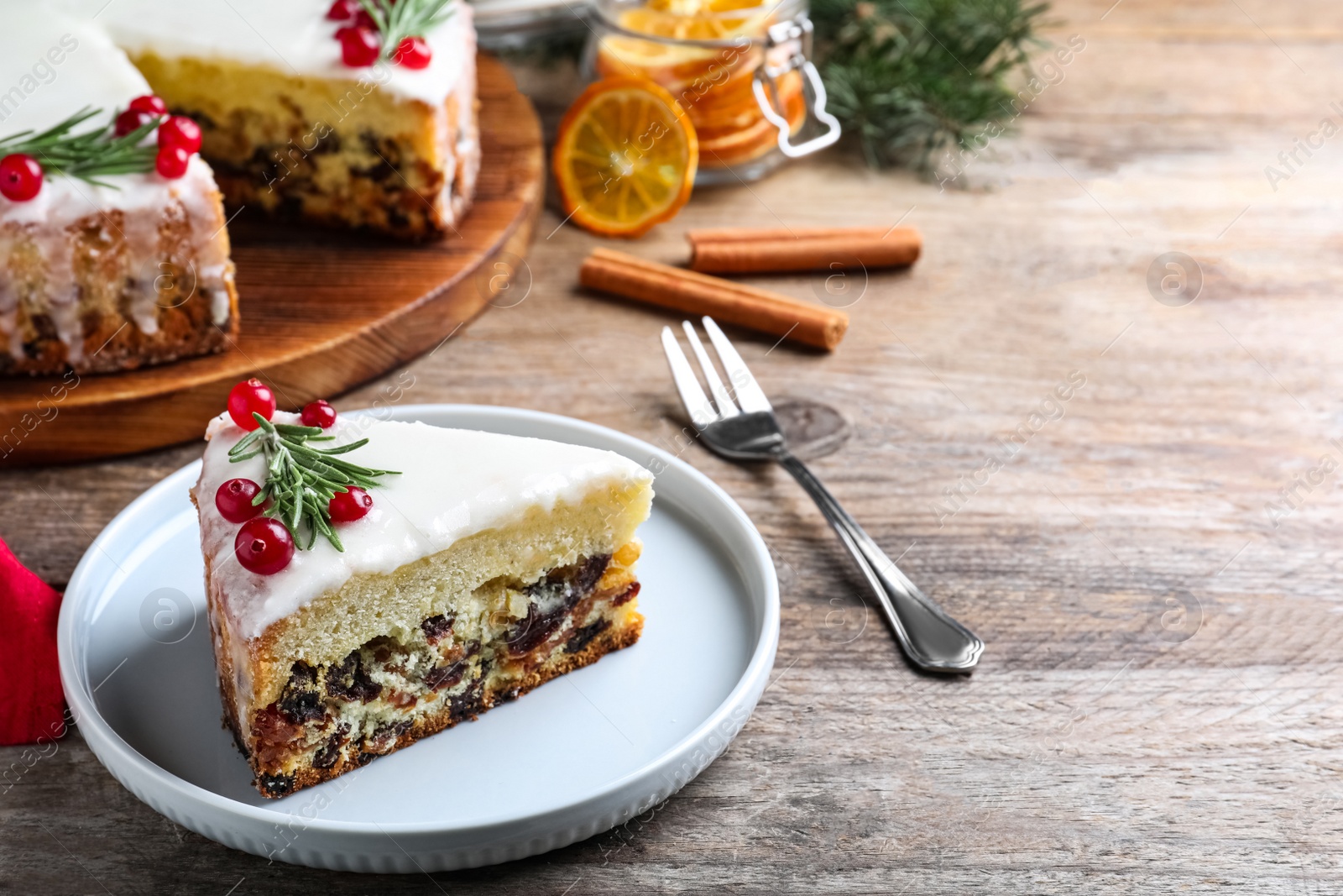 Photo of Slicetraditional Christmas cake decorated with rosemary and cranberries on wooden table