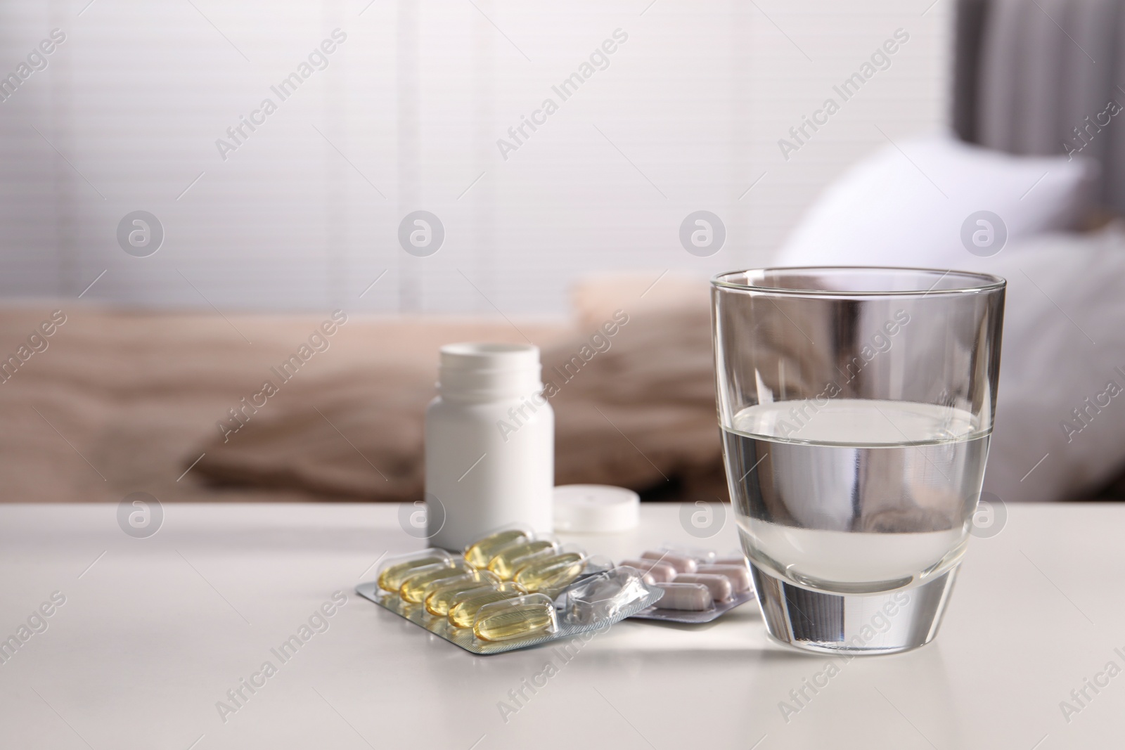 Photo of Glass of water, different pills in blisters and medical bottle on white table indoors, space for text