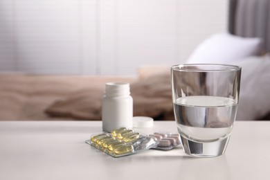 Glass of water, different pills in blisters and medical bottle on white table indoors, space for text
