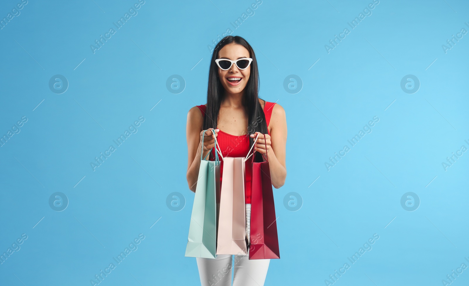 Photo of Beautiful young woman with paper shopping bags on light blue background