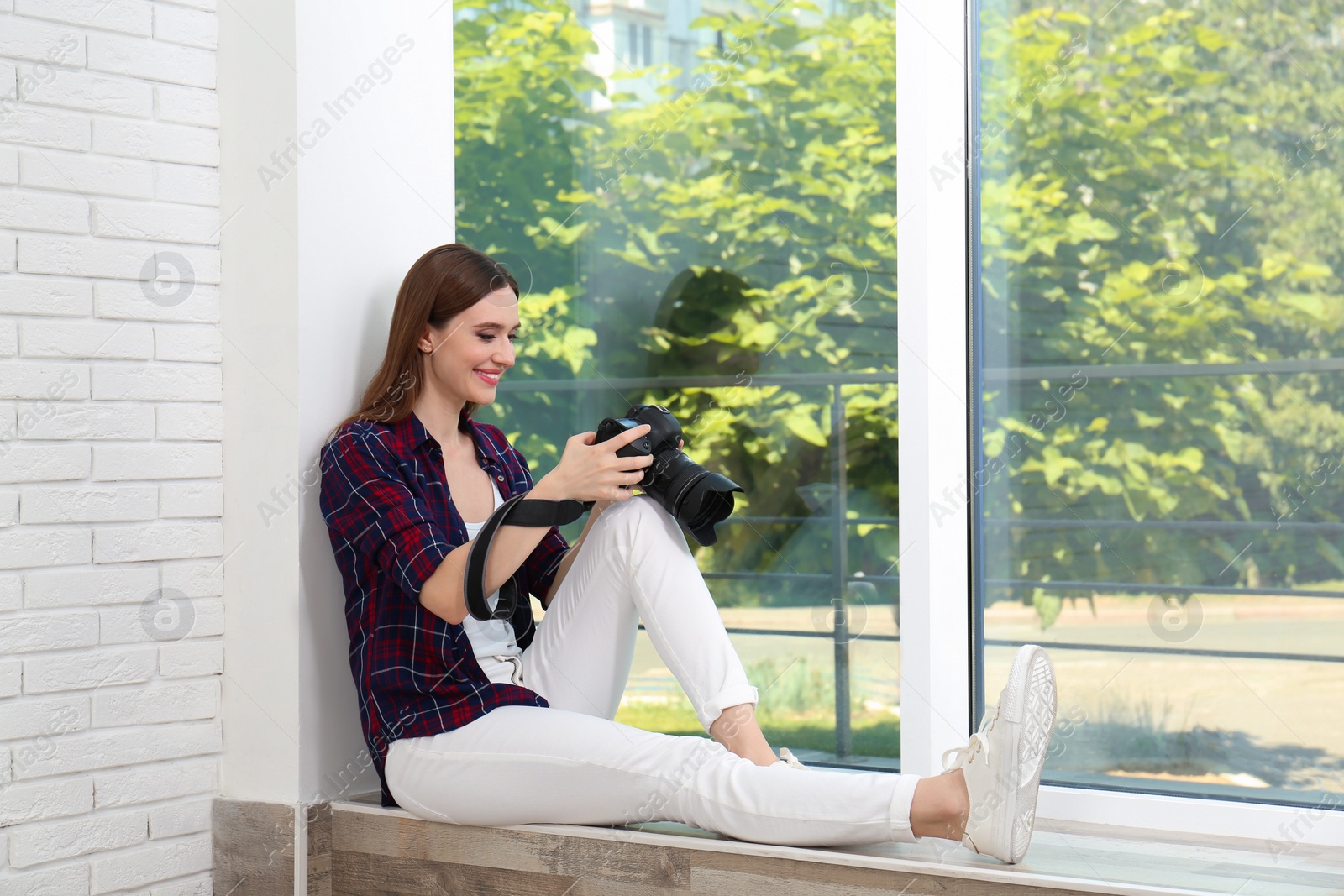 Photo of Professional photographer with modern camera sitting near window indoors