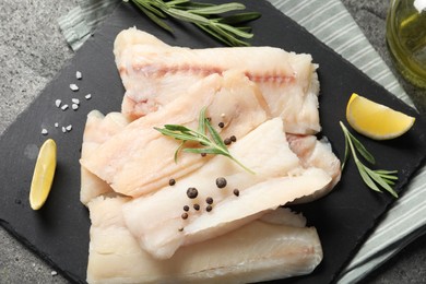 Photo of Pieces of raw cod fish, rosemary, peppercorns and lemon on grey table, top view