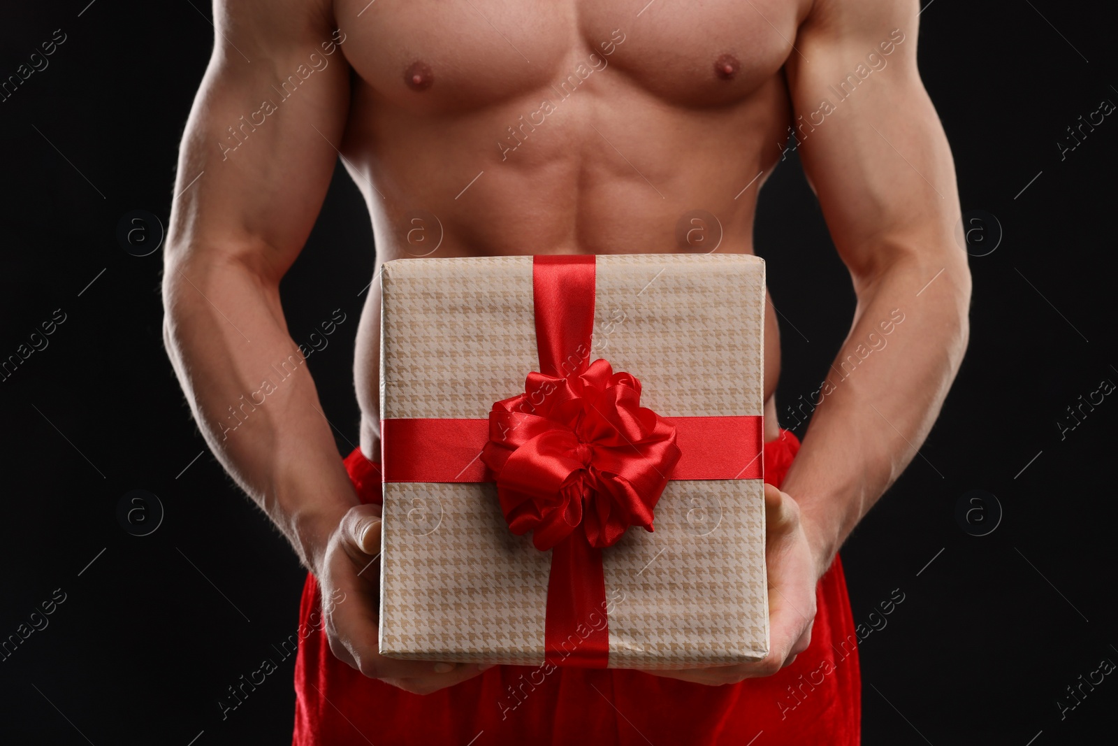 Photo of Attractive young man with muscular body holding Christmas gift box on black background, closeup