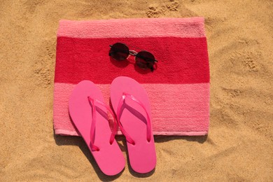 Beach towel with slippers and sunglasses on sand, flat lay