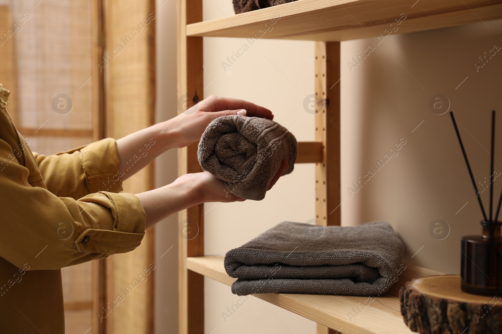 Photo of Woman putting rolled towel onto shelf indoors, closeup