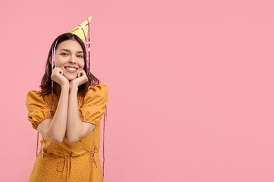 Happy young woman in party hat on pink background