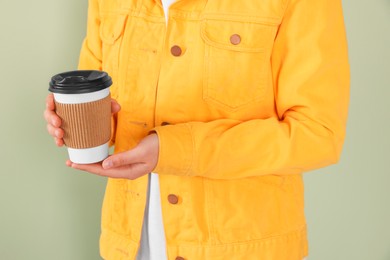 Photo of Woman holding takeaway cup with drink on pale green background, closeup. Coffee to go