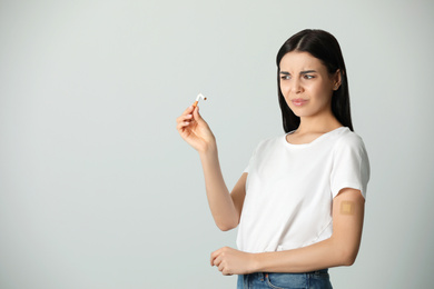 Photo of Emotional young woman with nicotine patch and cigarette on light grey background. Space for text