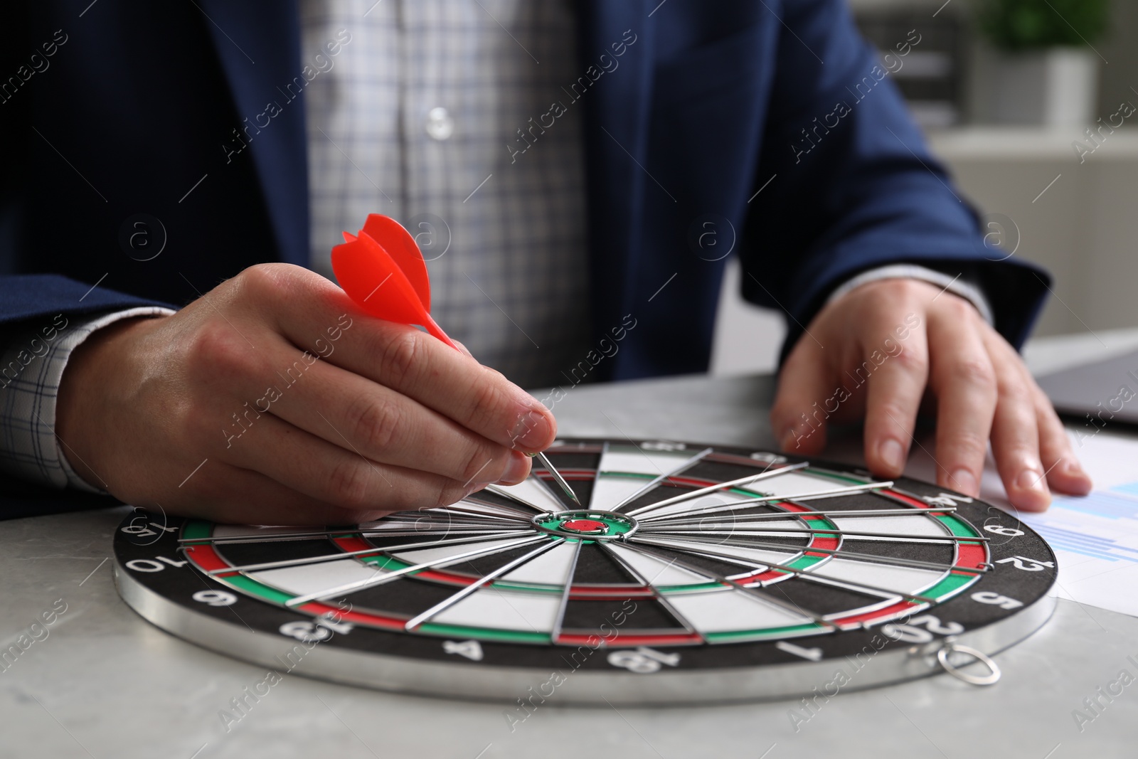 Photo of Business targeting concept. Man with dart aiming at dartboard at table indoors, closeup