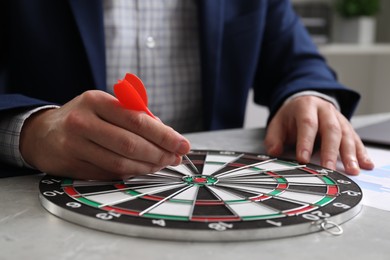 Business targeting concept. Man with dart aiming at dartboard at table indoors, closeup