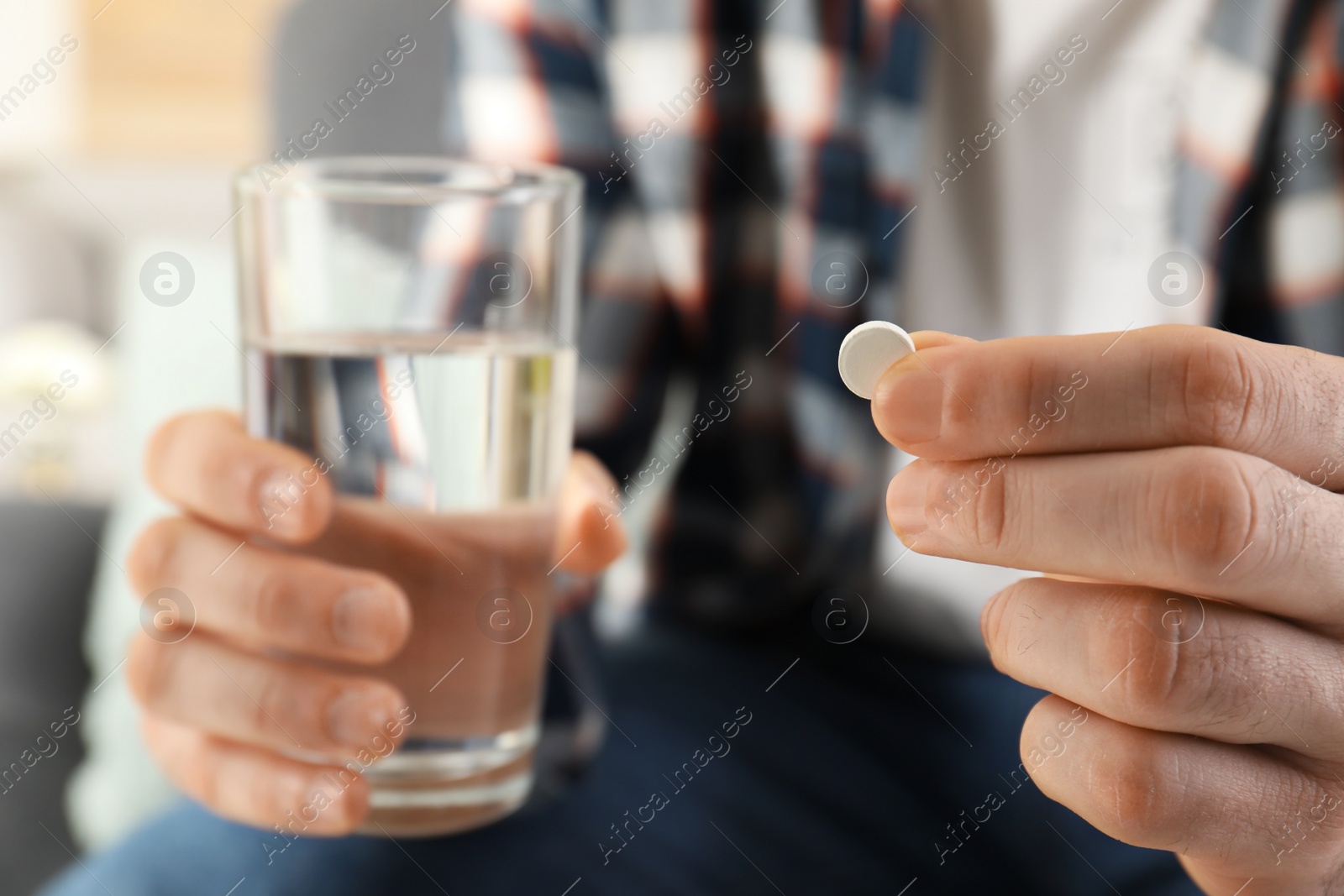 Photo of Man holding pill and glass of water indoors, closeup