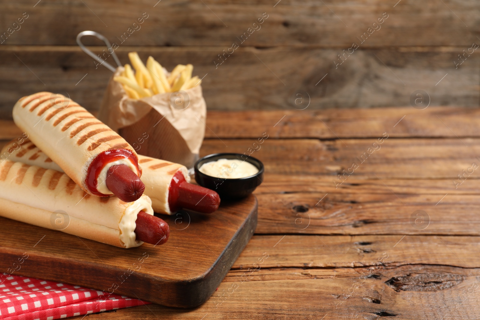Photo of Delicious french hot dogs, fries and dip sauce on wooden table. Space for text
