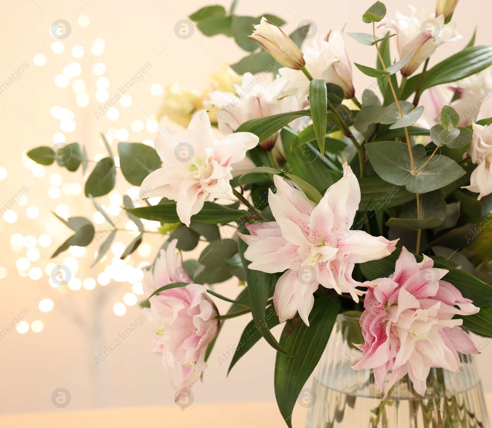 Photo of Bouquet of beautiful lily flowers in vase against beige background with blurred lights, closeup