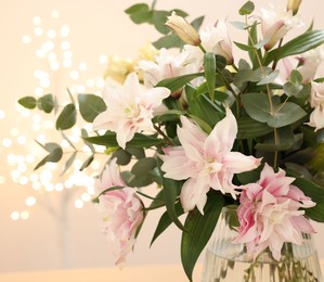 Bouquet of beautiful lily flowers in vase against beige background with blurred lights, closeup